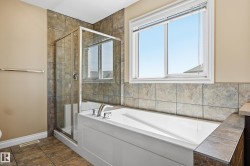 Bathroom featuring a white bathtub, glass-enclosed shower, polished chrome fixtures, and natural stone-look tile flooring - 