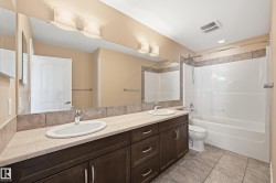 Bathroom featuring a dual vanity with undermount sinks and dark wood-finish cabinetry, a full-width mirror, and a combination shower/tub with tile surround - 
