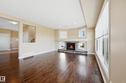 Spacious living area featuring rich wood-finish flooring, a corner stone fireplace with a substantial mantel, and recessed lighting - 