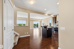 Open-concept interior featuring wood-finish flooring, a kitchen island with seating, stainless steel appliances, and a sliding glass door to the exterior - 