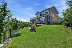 Expansive rear lawn featuring a black wrought iron fence, mature trees, and a stone planter - 