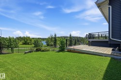 Expansive backyard featuring a manicured lawn, a wooden deck with black metal railings, and a black metal fence bordering a natural area with a pond - 