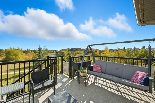 Expansive outdoor balcony featuring a concrete surface, black metal railings, and a backdrop of green space with a visible body of water - 1590 Chapman Way, Edmonton, AB 