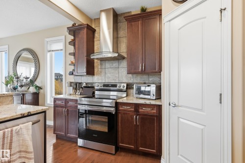 Kitchen featuring dark wood cabinetry, stainless steel appliances, granite countertops, tile backsplash, and wood-finish flooring - 1590 Chapman Way, Edmonton, AB 