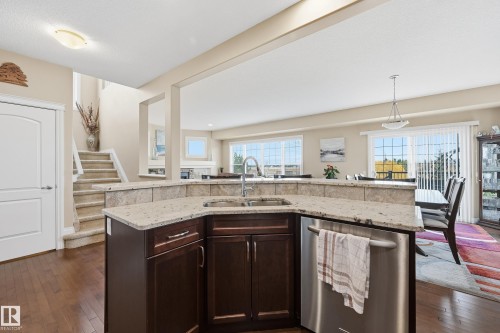 Kitchen island featuring granite countertops, a stainless steel sink with a gooseneck faucet, and integrated dishwasher - 1590 Chapman Way, Edmonton, AB 