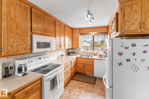 Kitchen featuring wood cabinetry, white appliances, a tiled backsplash, and a double basin sink beneath a window - 4611 Lakeshore Drive, Bonnyville Town, AB - Indoor Photo Showing Kitchen With Double Sink