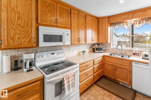 Kitchen featuring natural wood cabinetry, a tile backsplash, and light-toned countertops - 4611 Lakeshore Drive, Bonnyville Town, AB - Indoor Photo Showing Kitchen With Double Sink
