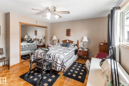 Bedroom featuring a full-length mirrored closet, wood-finish parquet flooring, a ceiling fan with integrated lighting, and a large window with natural light - 4611 Lakeshore Drive, Bonnyville Town, AB - Indoor Photo Showing Bedroom