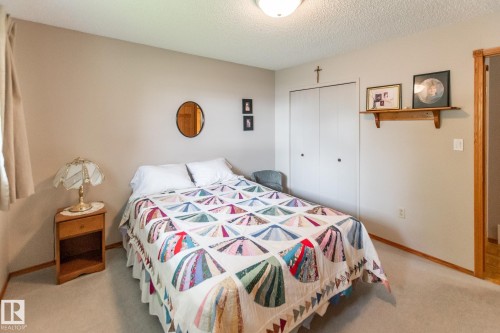 Carpeted room featuring a window with drapes, a corner nightstand with a drawer, and a built-in closet with bi-fold doors - 4611 Lakeshore Drive, Bonnyville Town, AB - Indoor Photo Showing Bedroom
