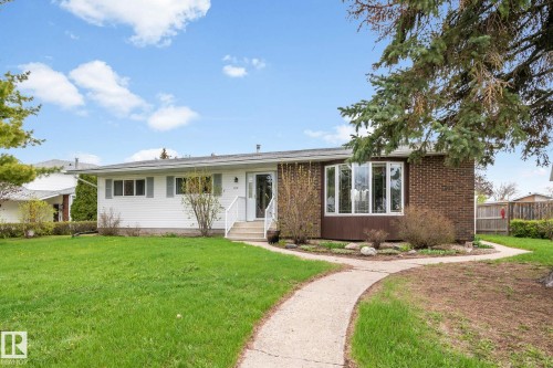 Exterior featuring a white siding facade, a brick-clad section with a bay window, a concrete pathway, and a mature front lawn - 4611 Lakeshore Drive, Bonnyville Town, AB - Outdoor