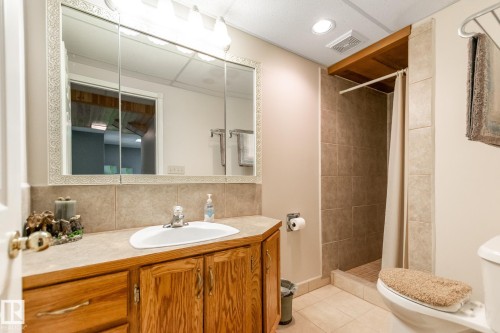 Bathroom featuring a tiled shower stall with a neutral shower curtain, wood-finish vanity with an integrated sink, and a large medicine cabinet with an ornate frame - 4611 Lakeshore Drive, Bonnyville Town, AB - Indoor Photo Showing Bathroom