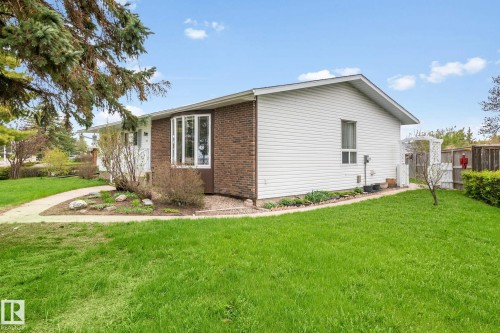 Exterior featuring brick and white siding, a bay window, a concrete walkway, mature trees, and a grassy lawn - 4611 Lakeshore Drive, Bonnyville Town, AB - Outdoor