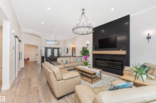 Spacious living area featuring light wood-finish flooring, a contemporary black shiplap accent wall with a built-in linear fireplace, a light wood mantle, and an overhead chandelier - 627 Forest Lane, Edmonton, AB - Indoor Photo Showing Living Room With Fireplace