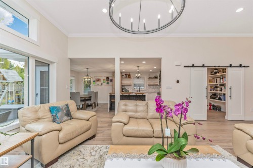 Vaulted ceiling living room featuring wood-finish flooring, a contemporary chandelier, a large sliding glass door, and a barn door pantry - 627 Forest Lane, Edmonton, AB - Indoor Photo Showing Living Room