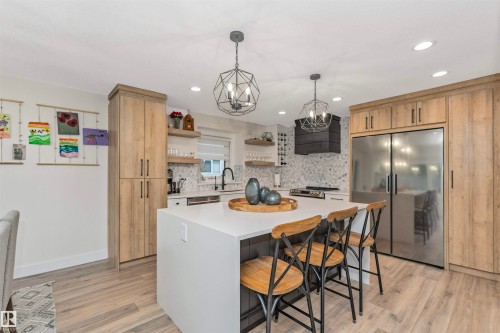 Kitchen featuring a large waterfall-edge island with seating, integrated stainless steel appliances, wood-finish cabinetry, and recessed lighting - 627 Forest Lane, Edmonton, AB - Indoor Photo Showing Kitchen