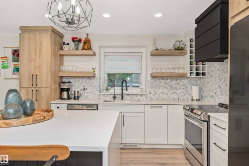 Gourmet kitchen featuring a solid surface countertop island, white cabinetry with matte black hardware, light wood-finish flooring, a mosaic tile backsplash, and stainless steel appliances - 627 Forest Lane, Edmonton, AB - Indoor Photo Showing Kitchen With Upgraded Kitchen
