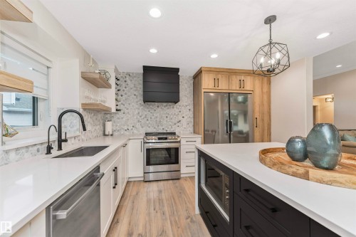 Modern kitchen featuring white perimeter cabinetry, a black kitchen island with a built-in microwave, light wood-finish flooring, and a stainless steel appliance suite - 627 Forest Lane, Edmonton, AB - Indoor Photo Showing Kitchen With Upgraded Kitchen