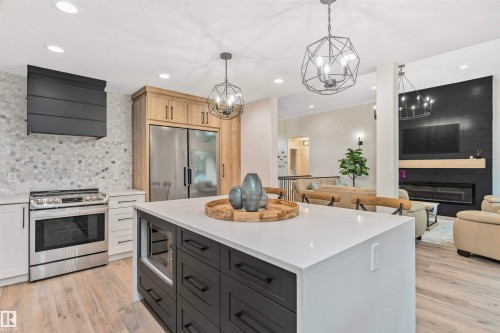 Contemporary kitchen featuring a large island with integrated microwave, stainless steel appliances, mosaic tile backsplash, and wood-finish flooring - 627 Forest Lane, Edmonton, AB - Indoor Photo Showing Kitchen With Upgraded Kitchen