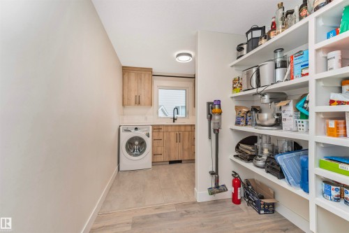 Laundry area with a built-in washing machine, light wood-finish cabinetry, and a single basin sink with a black faucet - 627 Forest Lane, Edmonton, AB - Indoor Photo Showing Laundry Room