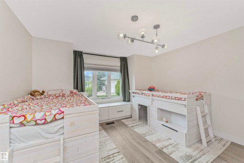 Spacious room featuring wood-finish flooring, a contemporary linear chandelier, and a large window with a built-in window seat and integrated storage drawers - 627 Forest Lane, Edmonton, AB - Indoor Photo Showing Bedroom