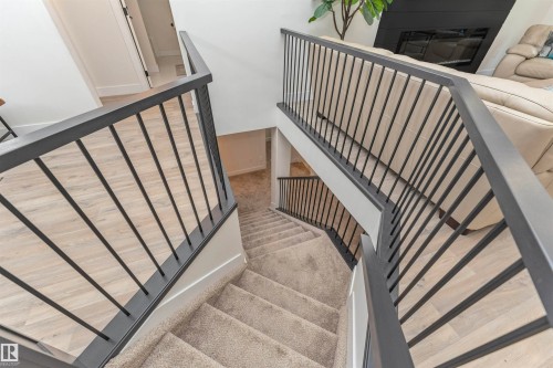 Multi-level interior featuring a carpeted staircase with dark metal railings, light wood-finish flooring, white walls, and bright overhead lighting - 627 Forest Lane, Edmonton, AB -  Photo Showing Other Room