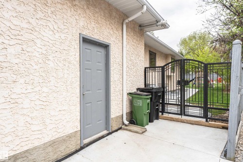 Stucco exterior with a side entry door, concrete patio, and decorative wrought iron fencing providing access to the grassy yard - 627 Forest Lane, Edmonton, AB - Outdoor With Exterior