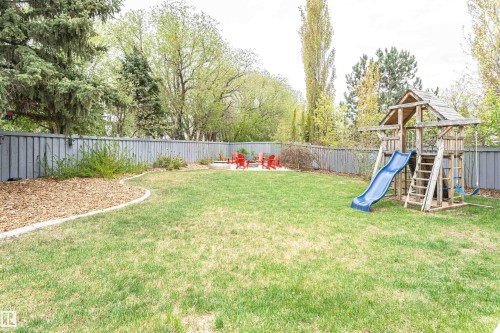 Spacious backyard featuring a manicured lawn, a full privacy fence, mature trees, and a dedicated fire pit area - 627 Forest Lane, Edmonton, AB - Outdoor With Backyard