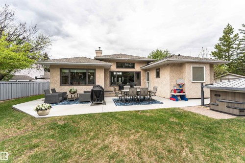 Expansive concrete patio with multiple outdoor living areas, complemented by a stucco exterior and dark-framed windows - 627 Forest Lane, Edmonton, AB - Outdoor With Deck Patio Veranda