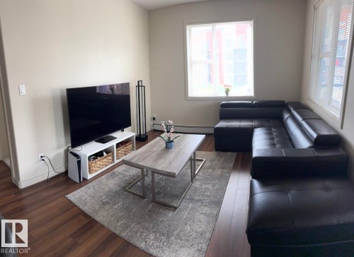 Spacious living area featuring wood-finish flooring, two large windows with blinds, and neutral wall tones - 228 308 Ambleside Link Sw, Edmonton, AB - Indoor Photo Showing Living Room