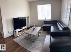 Spacious living area featuring wood-finish flooring, two large windows with blinds, and neutral wall tones - 