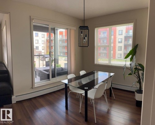 Dining area with wood-finish flooring, featuring a contemporary pendant light fixture and a large window with blinds - 228 308 Ambleside Link Sw, Edmonton, AB - Indoor Photo Showing Dining Room