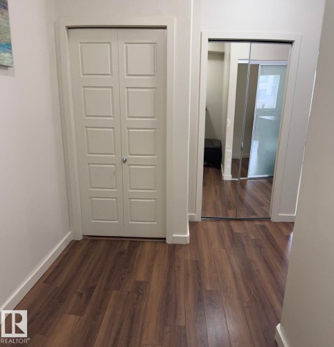 Hallway featuring wood-finish flooring, white baseboards, a bi-fold panel door, and mirrored sliding closet doors - 228 308 Ambleside Link Sw, Edmonton, AB - Indoor Photo Showing Other Room