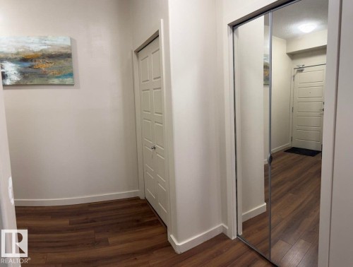 Entryway featuring wood-finish flooring, light-toned walls, and a mirrored closet door - 228 308 Ambleside Link Sw, Edmonton, AB - Indoor Photo Showing Other Room