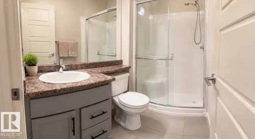 Full bathroom featuring a vanity with an integrated sink, patterned countertop, and gray cabinetry with black hardware - 228 308 Ambleside Link Sw, Edmonton, AB - Indoor Photo Showing Bathroom