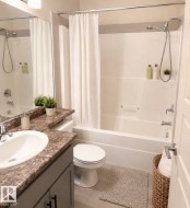 Contemporary bathroom featuring a combination shower and tub, a vanity with a stone-finish countertop, an undermount sink, a large wall-mounted mirror, and tile flooring - 