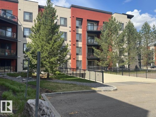 Modern apartment building with a red and beige facade, featuring multiple balconies with glass railings - 228 308 Ambleside Link Sw, Edmonton, AB - Outdoor With Balcony With Facade