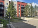Modern apartment building with a red and beige facade, featuring multiple balconies with glass railings - 228 308 Ambleside Link Sw, Edmonton, AB  - Outdoor With Balcony With Facade 