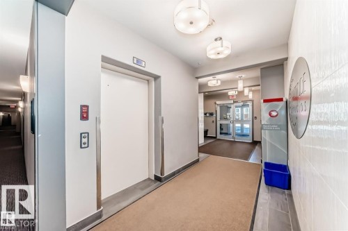 Building hallway featuring modern lighting fixtures and a carpeted floor - 228 308 Ambleside Link Sw, Edmonton, AB - Indoor Photo Showing Other Room