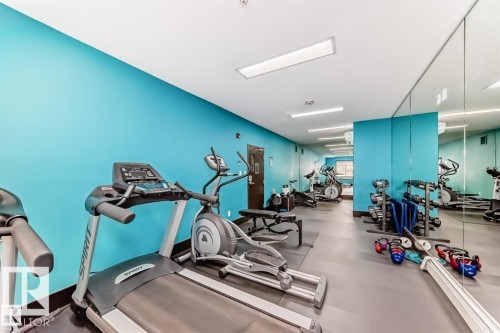 Fitness room with turquoise accent walls and extensive mirrored surfaces - 228 308 Ambleside Link Sw, Edmonton, AB - Indoor Photo Showing Gym Room