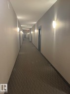 Hallway featuring recessed ceiling lighting, wall-mounted sconces, neutral wall finishes, patterned carpet flooring, and dark trim around doorways - 