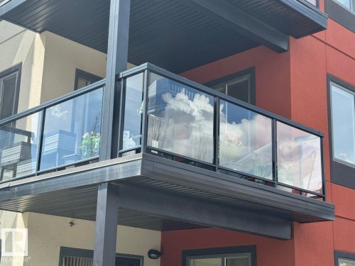 Balcony featuring clear glass railings with black framing, a dark gray soffit, and dark gray siding on the balcony base - 228 308 Ambleside Link Sw, Edmonton, AB -  With Exterior