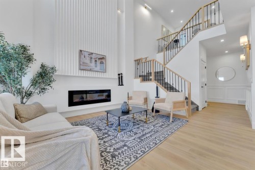 Open-concept living area featuring a two-story fireplace with a ribbed accent wall, wood-finish flooring, and a contemporary staircase with iron railings - 1129 Starling Drive, Edmonton, AB 
