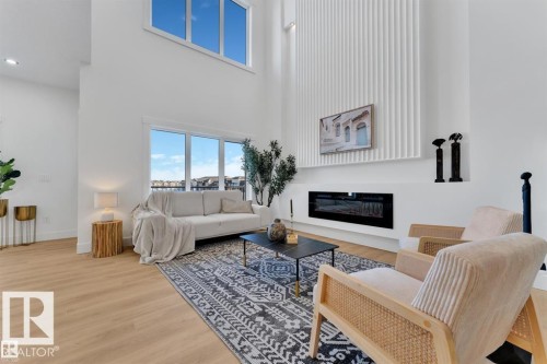 Two-story living area featuring wood-finish flooring, a contemporary fireplace, and a large window arrangement - 1129 Starling Drive, Edmonton, AB 
