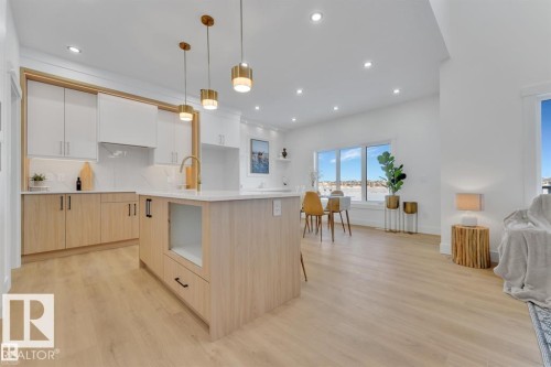 Contemporary kitchen featuring a large central island with countertop seating, two-tone cabinetry, brass hardware, and a white tile backsplash - 1129 Starling Drive, Edmonton, AB 