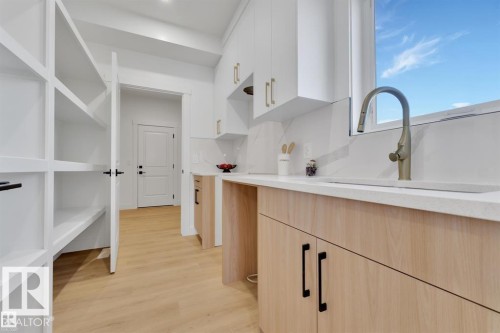 Spacious scullery featuring extensive white built-in shelving, light wood-finish flooring, white upper cabinetry, and a countertop with an undermount sink and a modern faucet - 1129 Starling Drive, Edmonton, AB 