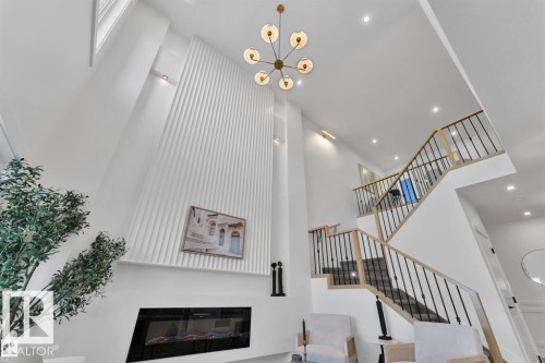 Vaulted ceiling featuring a contemporary chandelier, linear electric fireplace, and a two-story accent wall - 1129 Starling Drive, Edmonton, AB 