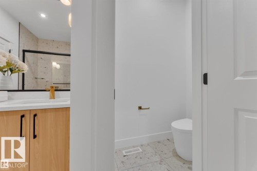 Modern bathroom featuring a wood-finish vanity with black hardware, a gold-tone faucet, and a white countertop with an integrated sink - 1129 Starling Drive, Edmonton, AB 