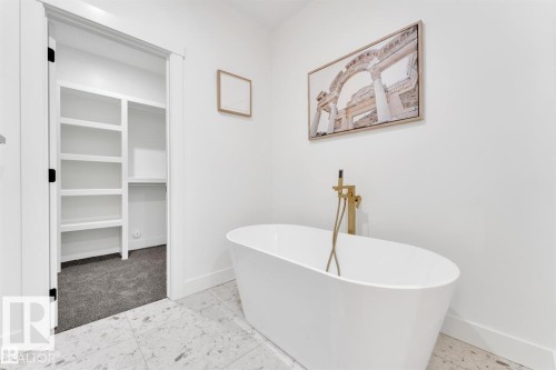 Freestanding soaking tub with gold-tone fixtures, complemented by white walls and light-toned tile flooring - 1129 Starling Drive, Edmonton, AB 