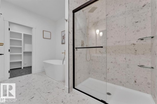 Spacious bathroom featuring a frameless glass shower enclosure with matte black hardware, a freestanding soaking tub, and large format terrazzo-style floor and wall tiling - 1129 Starling Drive, Edmonton, AB 