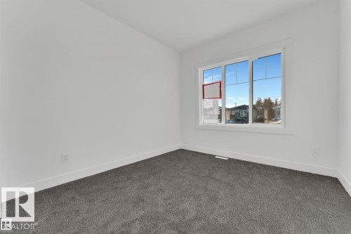 Bright room featuring a large multi-pane window, neutral white walls, and dark gray carpeting - 1129 Starling Drive, Edmonton, AB 